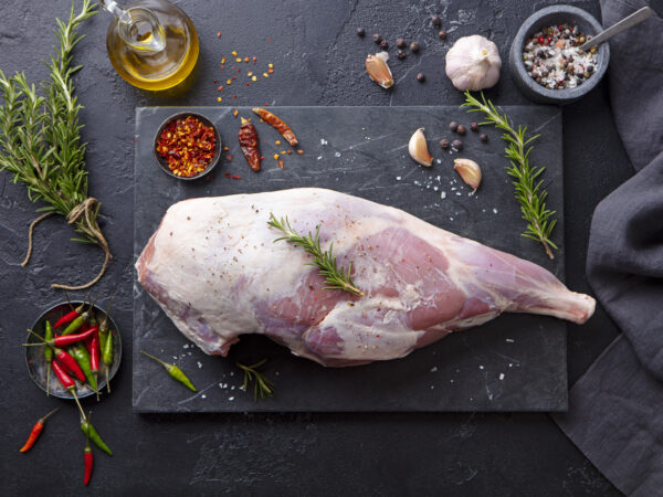 Raw lamb leg with spices and herbs on marble cutting board. Dark background. Top view. Lamb Leg